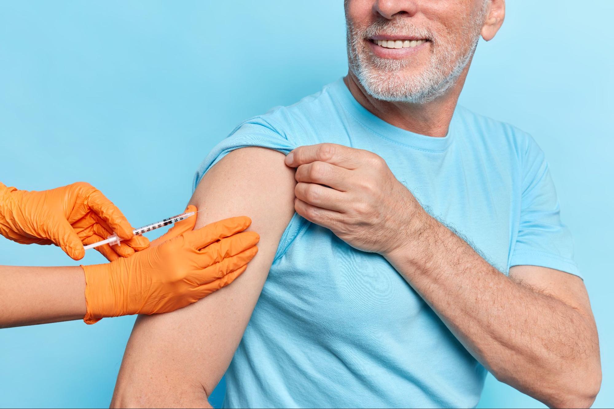 A cropped shot of a man in a casual T-shirt receiving a vitamin injection in his shoulder. 