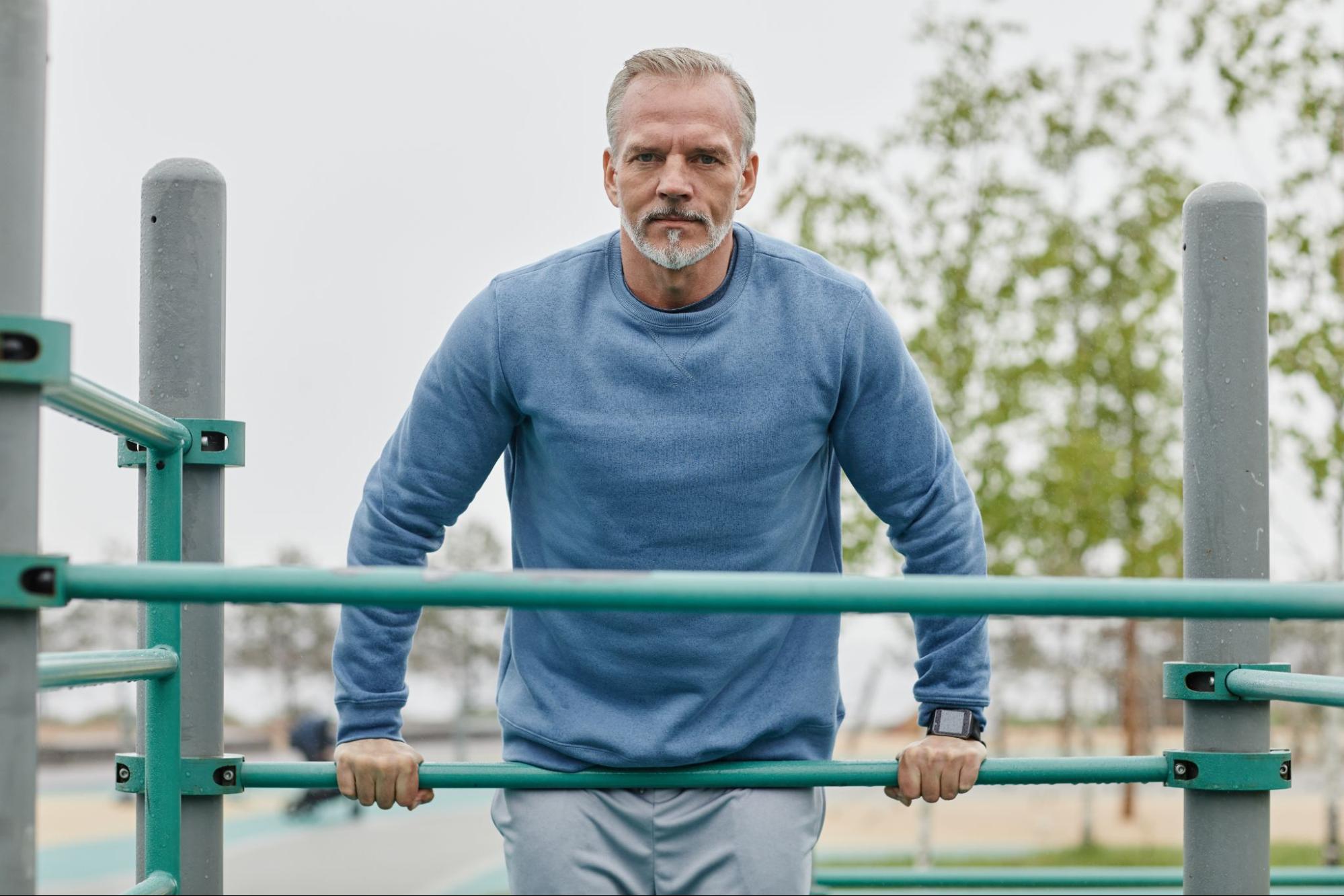 Senior man staying active on park fitness bars after starting HRT for men.
