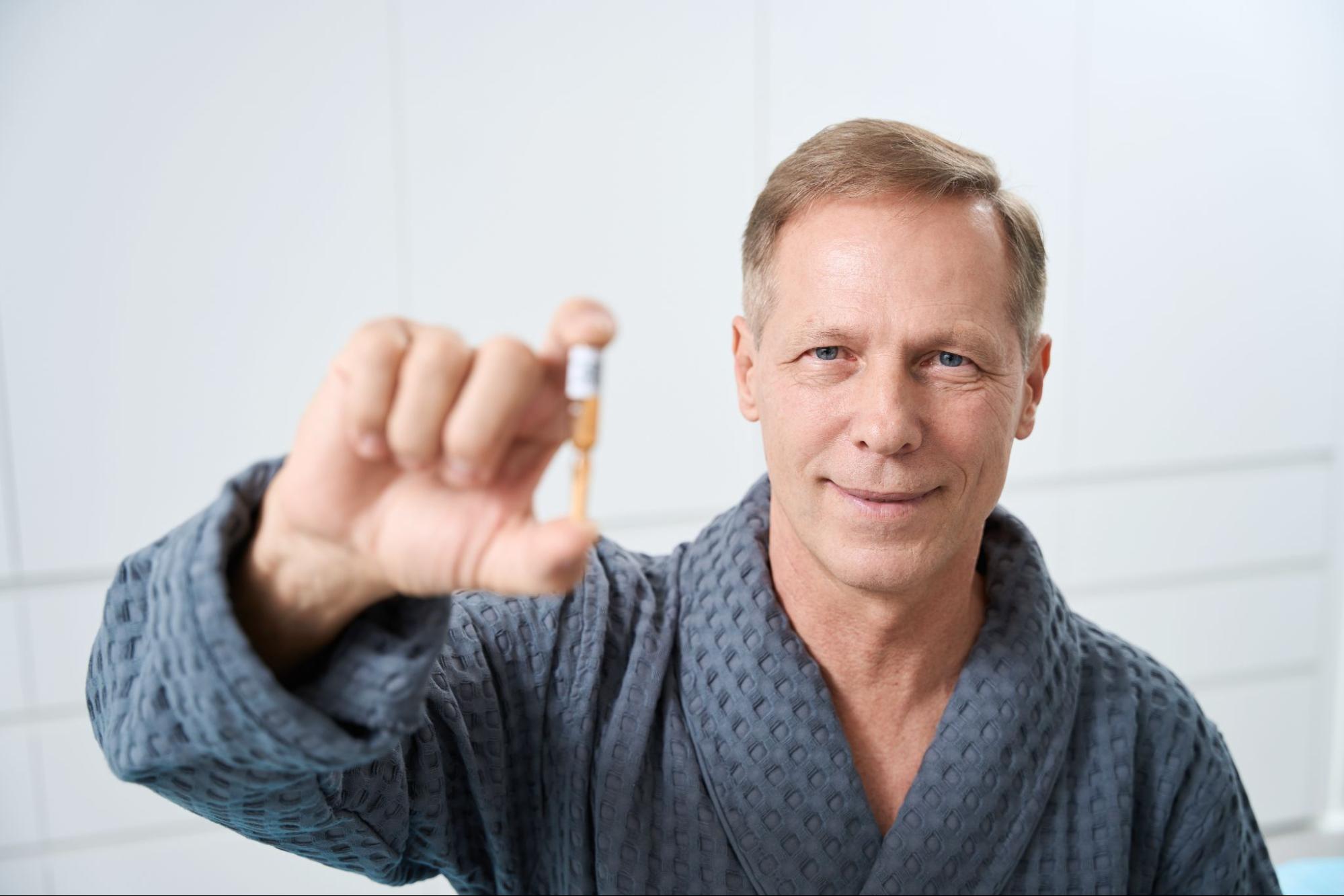 A middle-aged man is wearing a robe and holding up a capsule of medicine.