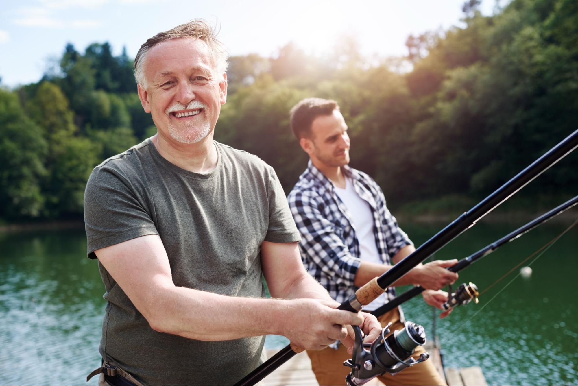 An old man is happily fishing with a younger man.