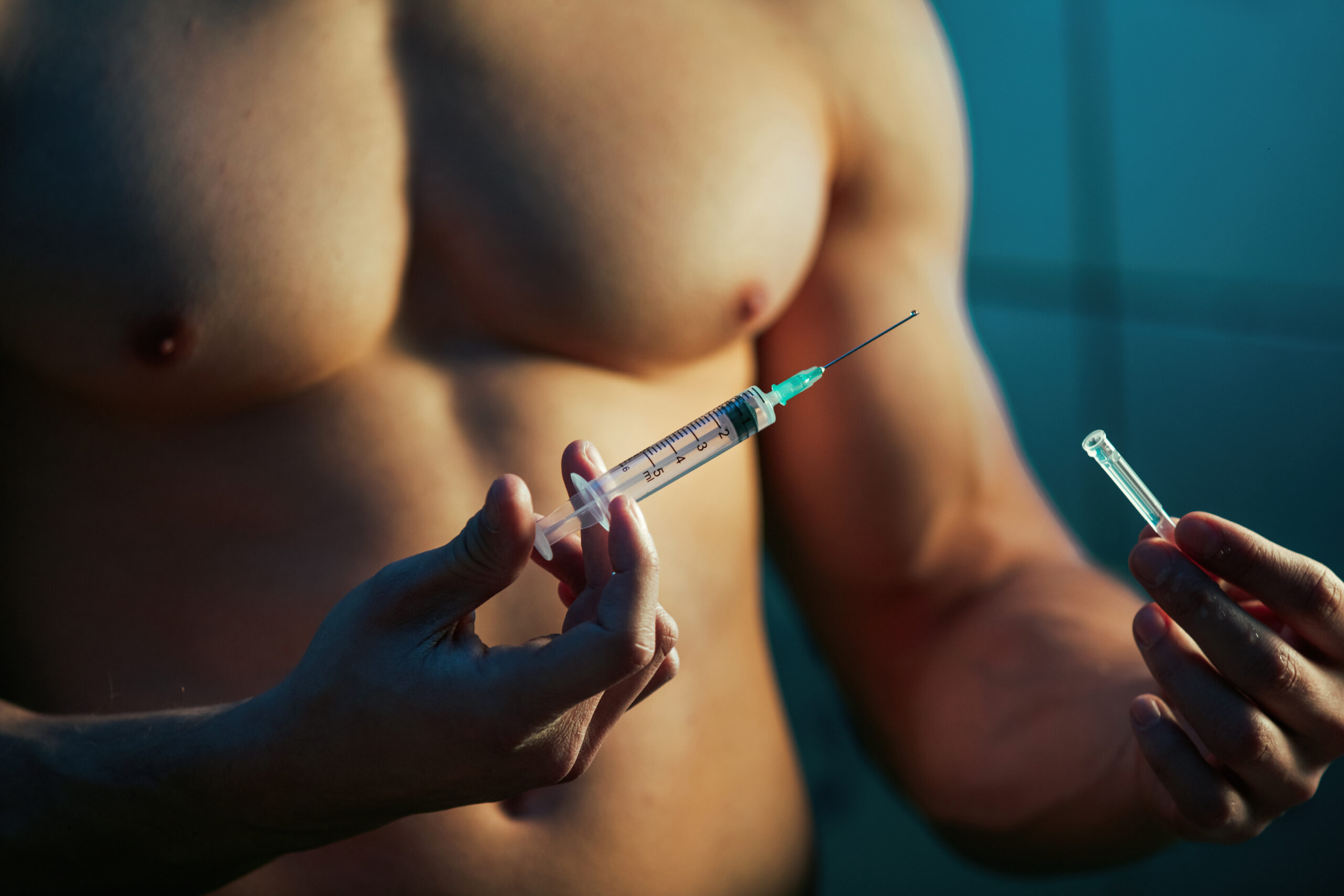 Closeup on a muscular man’s torso, holding a testosterone therapy syringe.