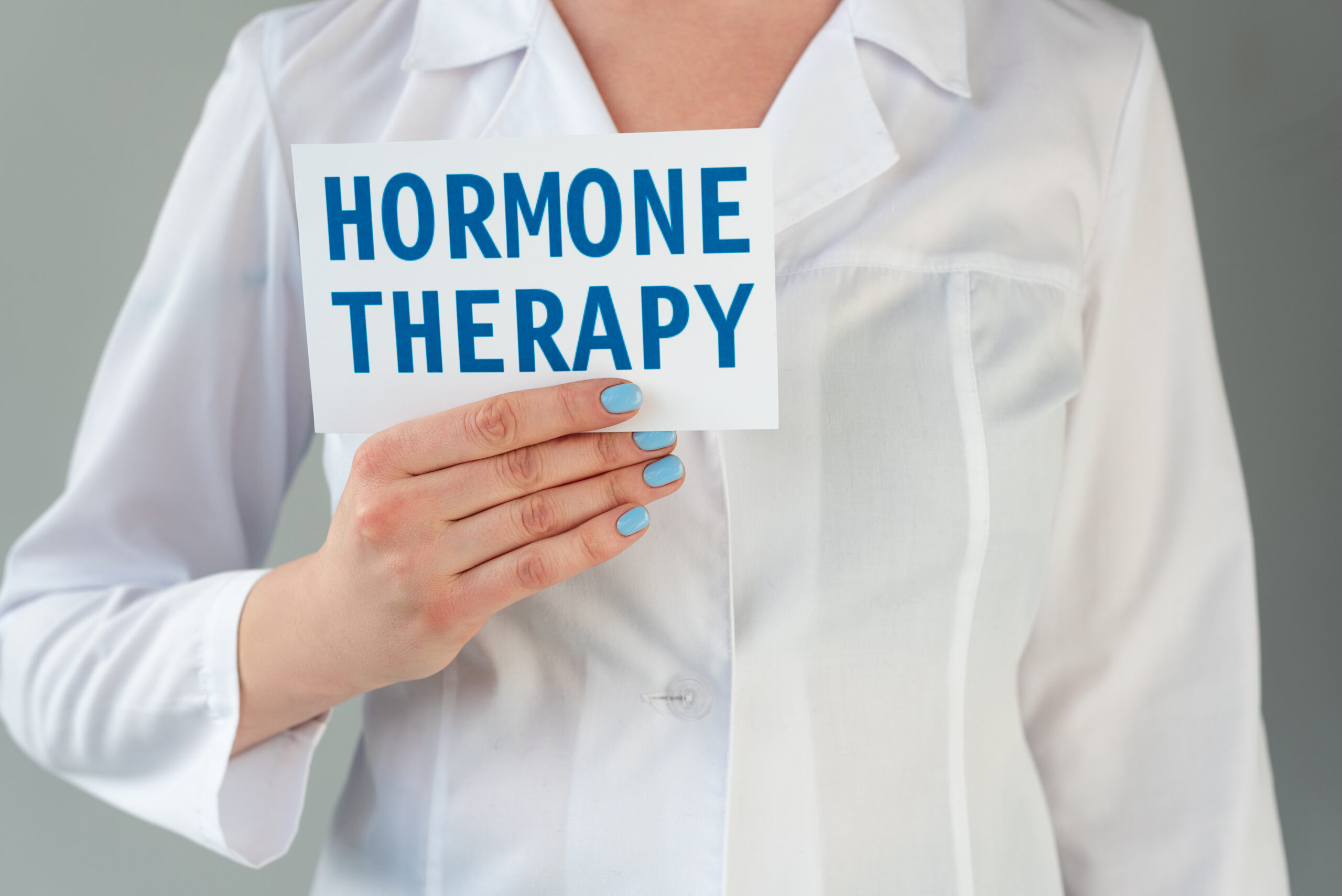 Cropped image of a doctor in a lab coat with a sign that reads “Hormone Therapy.”