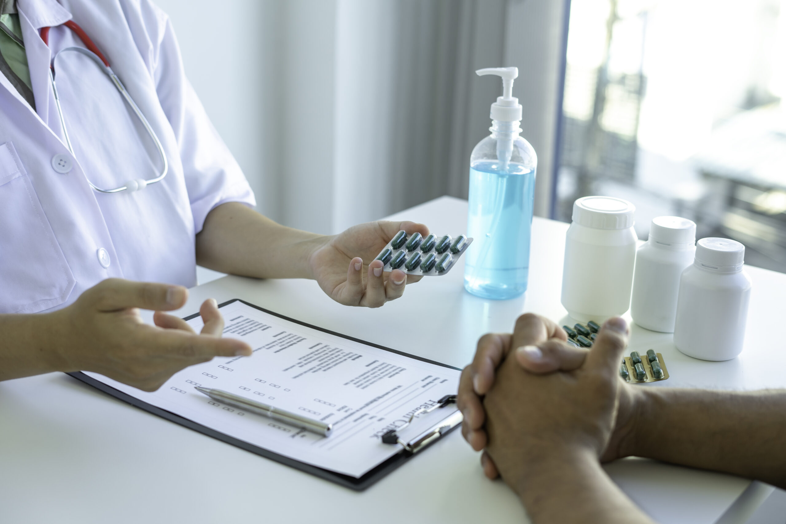 Zoomed in image of a doctor handing a patient a pack of pills over a desk.