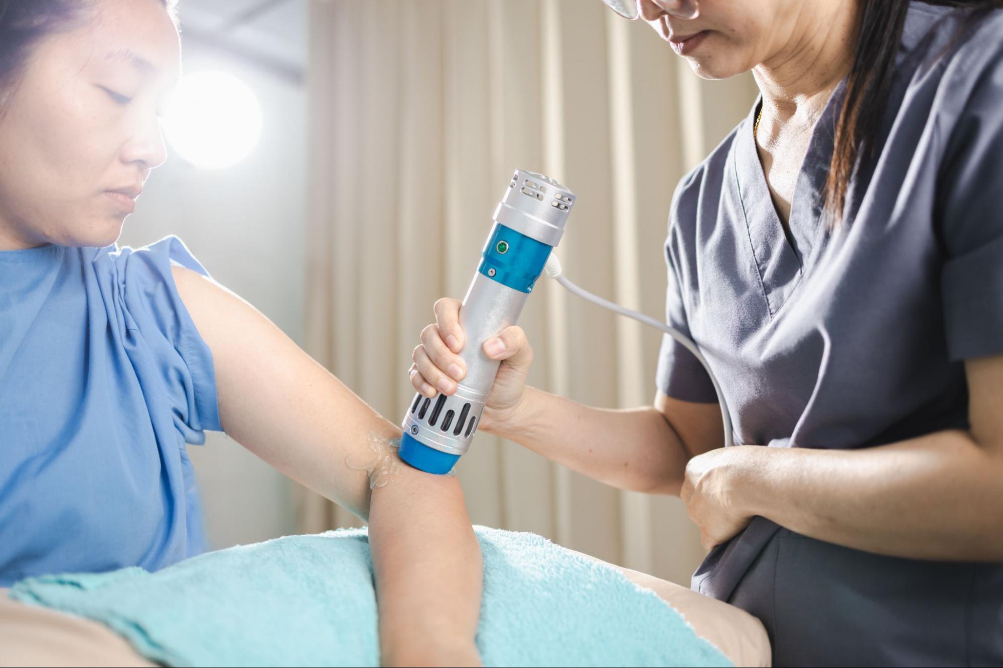 A medical professional administers shockwave therapy to their patient’s arm in an office.