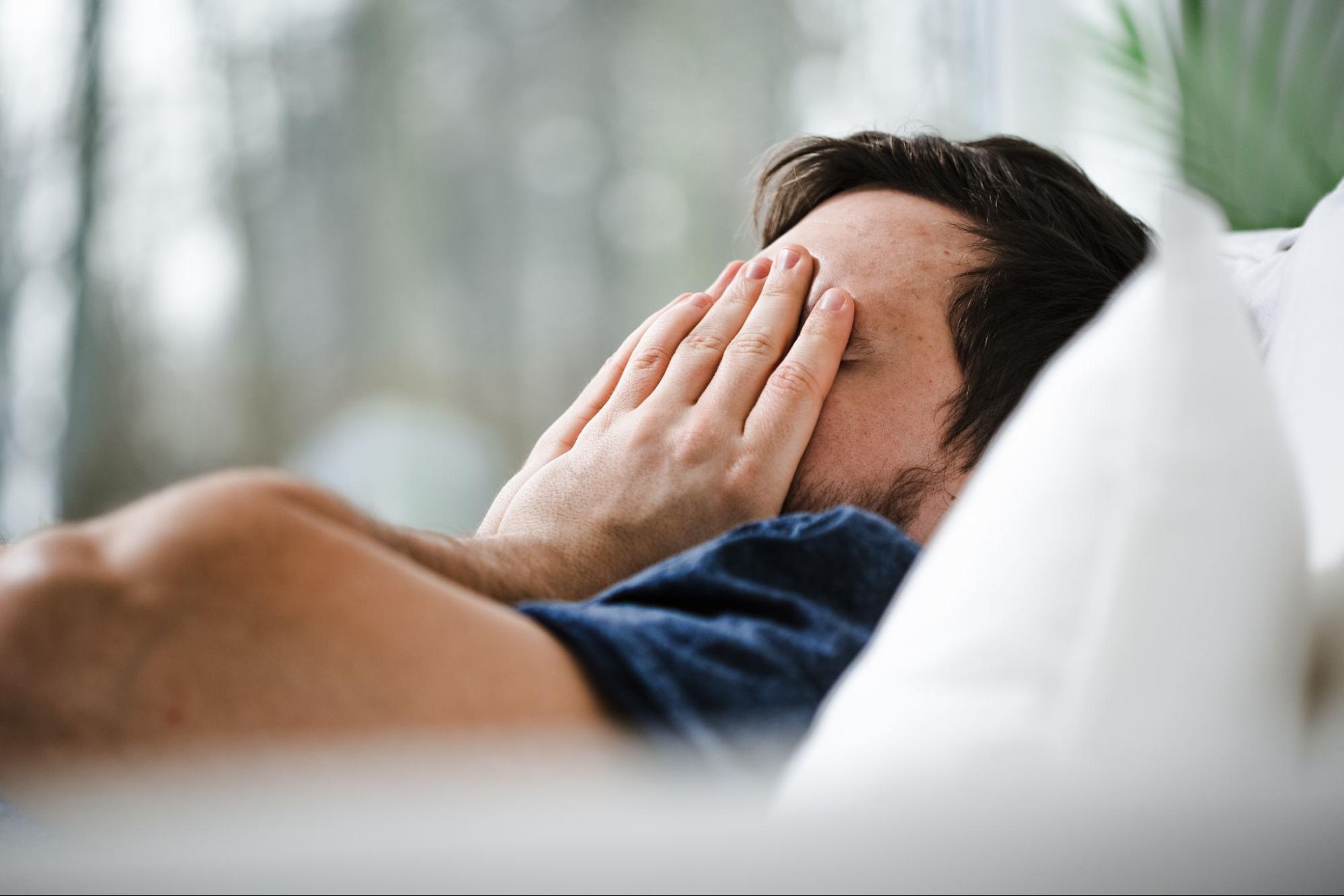 A man covers his face with his hands as he struggles to sleep.