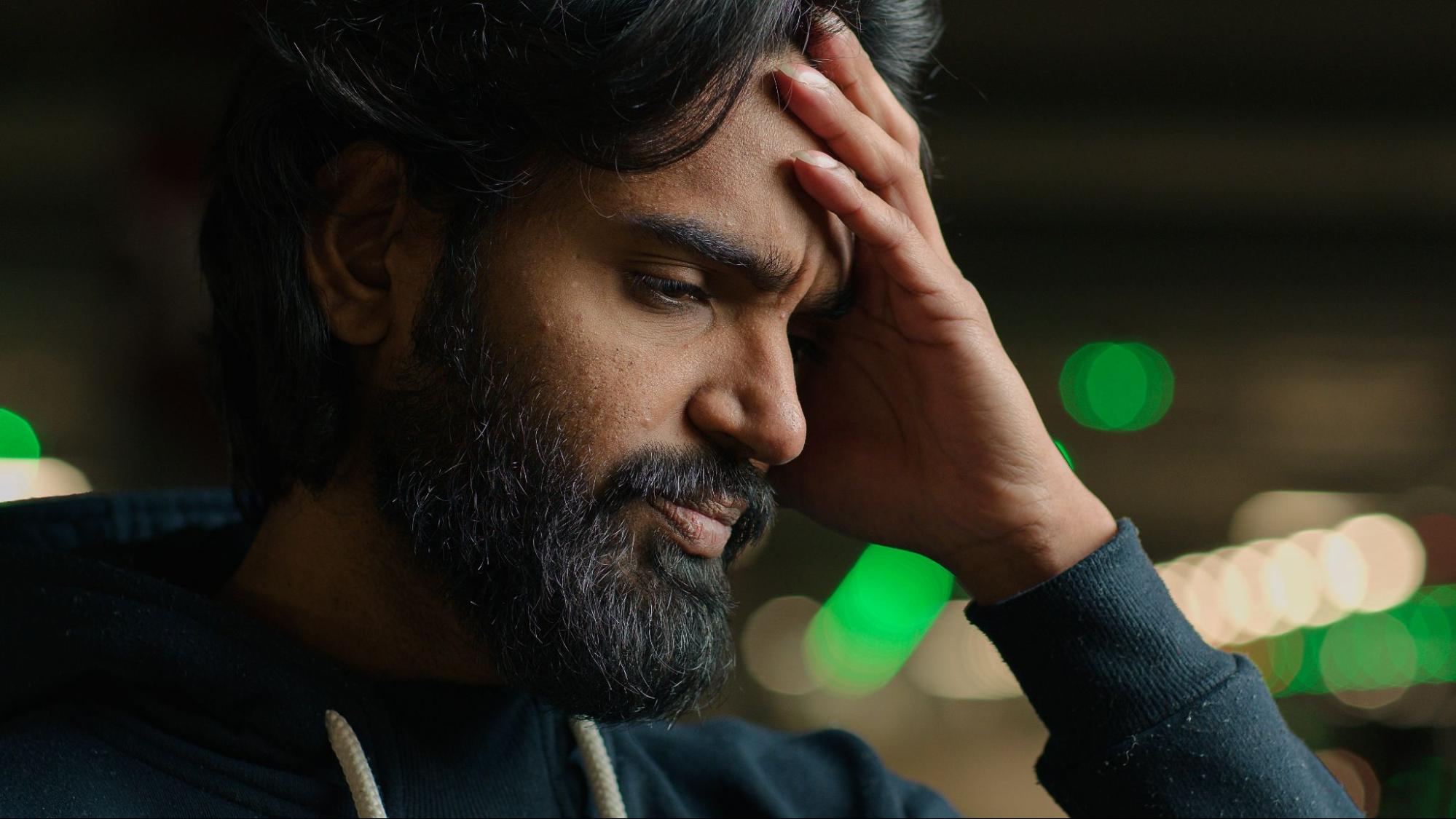 A sad, bearded Arabian man touches his forehead, looking stressed and anxious