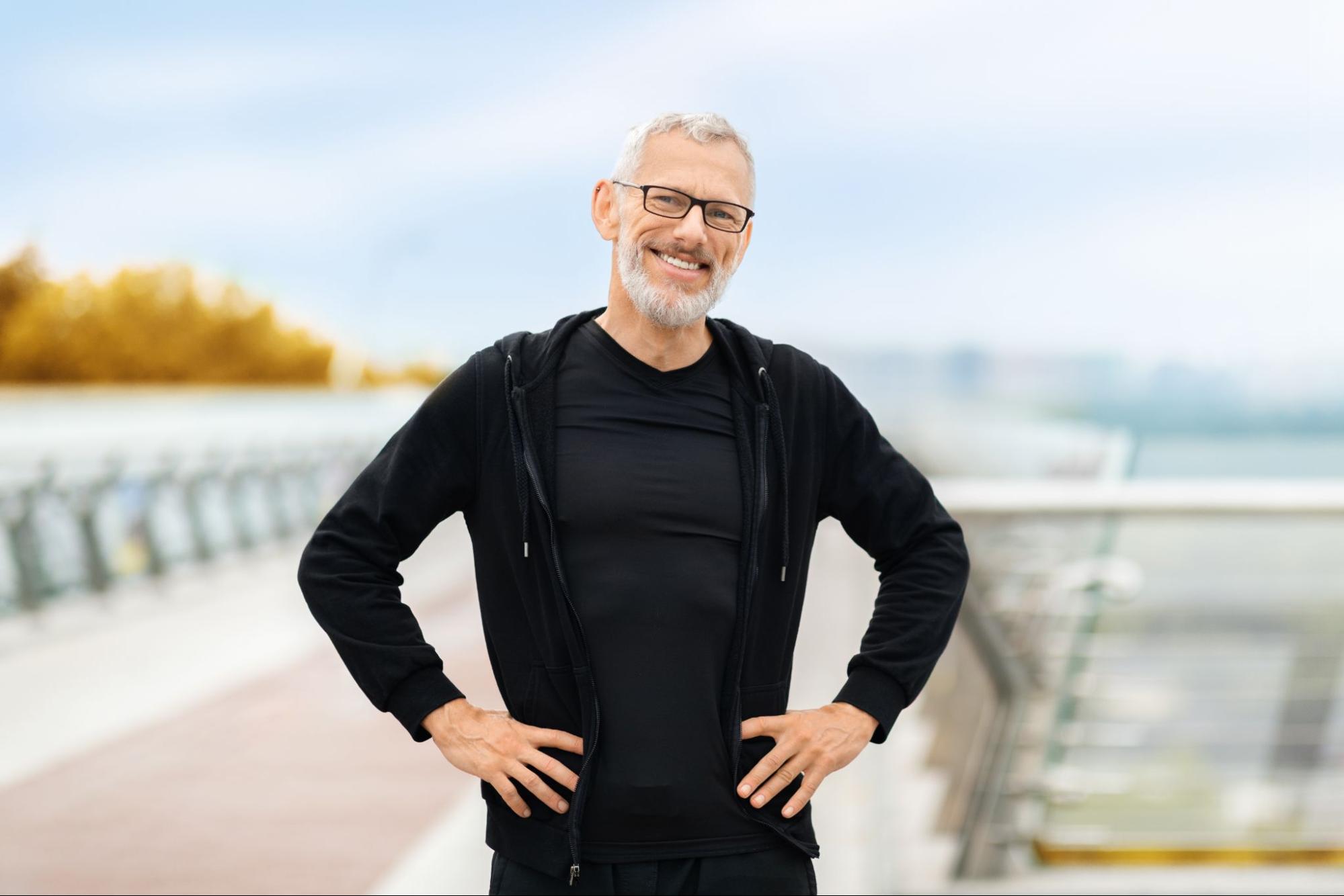An active senior man in black sports gear rests from jogging on a city street, showing vitality after hormone replacement therapy